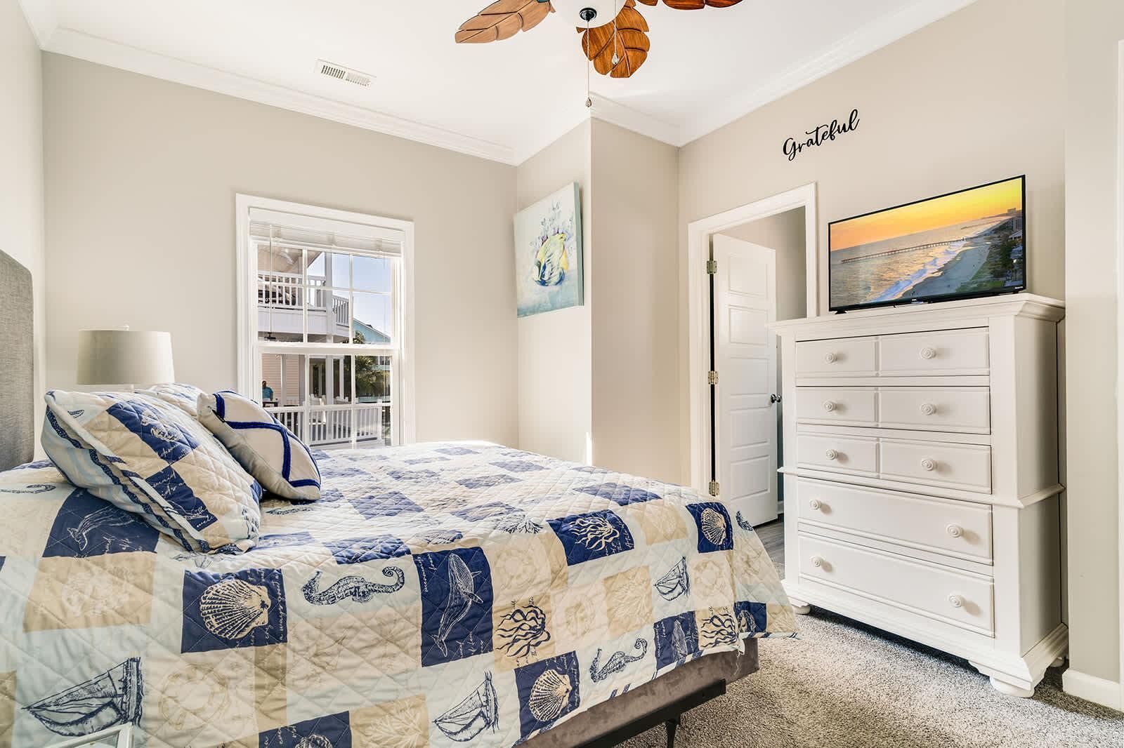 A bedroom with a bed, a dresser, a painting, and a view of a balcony.