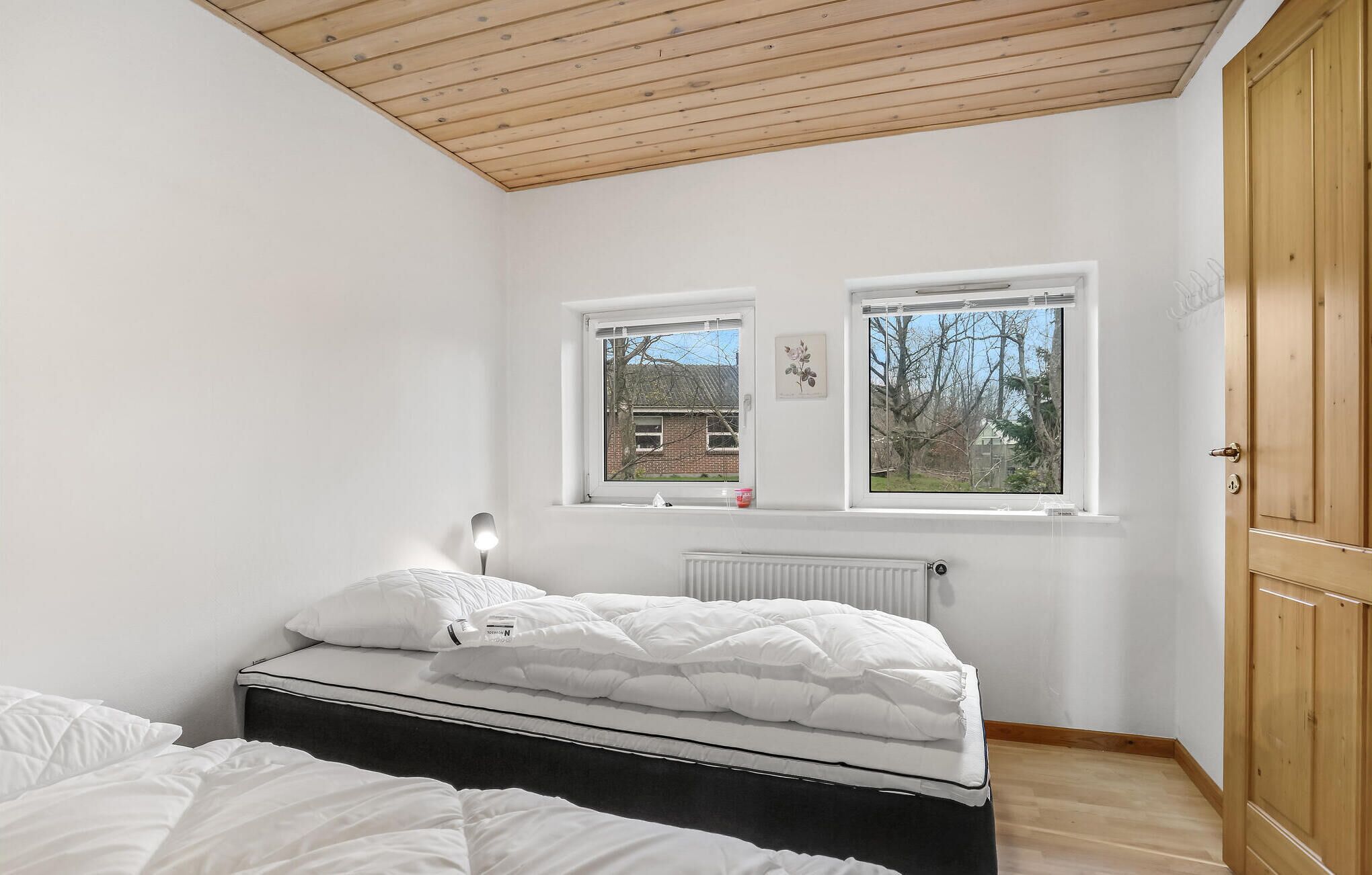 Une chambre à coucher avec un lit, deux fenêtres, un radiateur et une armoire en bois.