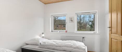Une chambre à coucher avec un lit, deux fenêtres, un radiateur et une armoire en bois.