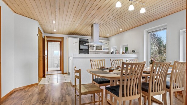 A modern kitchen with white cabinets, a central island, and a dining area with wooden chairs and a table.
