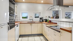 A modern kitchen with white cabinets, a stainless steel range hood, and a window overlooking a garden.