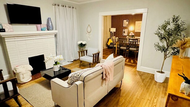 A living room with a white sofa, a coffee table, a fireplace, and a dining area in the background. - Stylish 3BR Home Sleeps 8 w/ Grill – Near CrossPlex & Downtown (Birmingham)