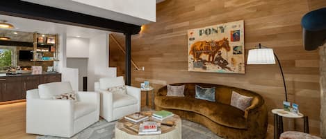 Una sala de estar moderna con chimenea, una obra de arte colgada de un caballo y una zona de estar acogedora con un sofá marrón y sillones blancos.