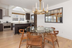 A modern kitchen with a central island, a round glass dining table, and wooden chairs.
