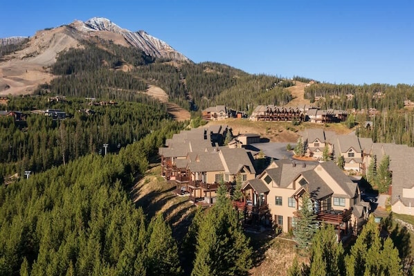 A resort with multiple buildings, surrounded by dense forests and a mountain in the background.