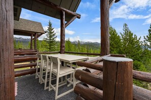 A wooden deck with a table and chairs, overlooking a mountainous landscape.