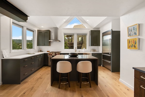 Una cocina moderna con una isla central, muebles oscuros y vistas amplias a través de grandes ventanales.