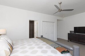 A bedroom with a bed, a ceiling fan, a dresser, and a television.