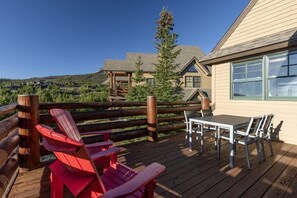 A wooden deck with red Adirondack chairs and a table, overlooking a mountainous landscape.
