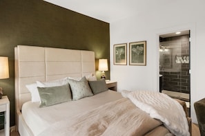 Habitación de hotel con una cama grande, una mesita de noche, una lámpara y un baño visible a través de una puerta abierta.