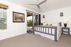 A bedroom with a bed, a ceiling fan, a window, and a door leading to an outdoor area.