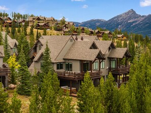 A cluster of log cabin-style lodges with multiple stories and balconies, surrounded by dense forest and mountains in the background. - Ski-In/Ski-Out 3 Bedroom Moonlight Basin (Big Sky)