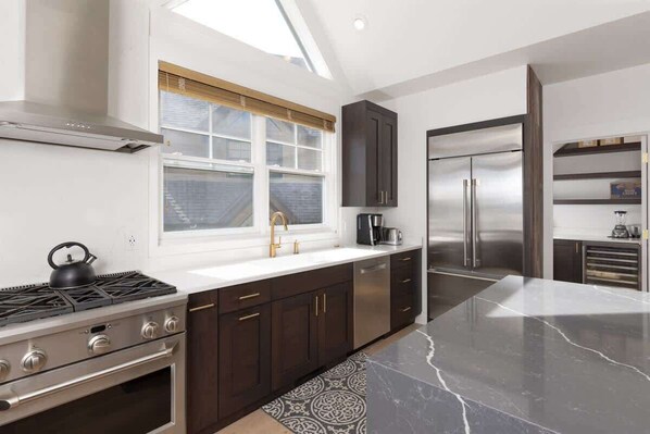 A modern kitchen with dark cabinetry, a stainless steel range, and a window with blinds.