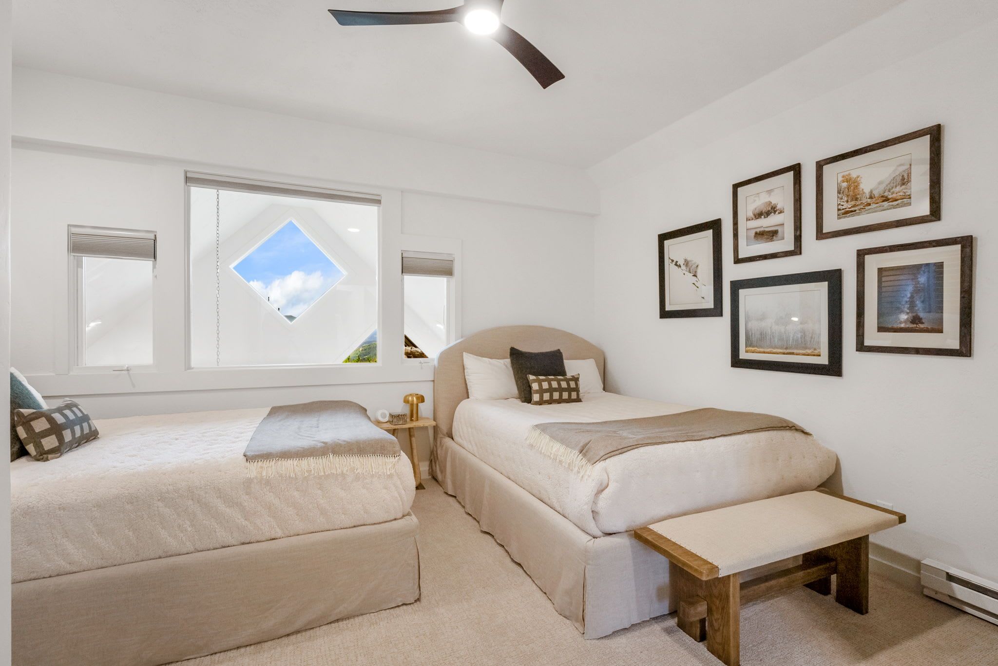 A bedroom with two beds, a bench, a ceiling fan, and a skylight.