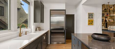A modern kitchen with a stainless steel refrigerator, a large window, and a wooden floor.