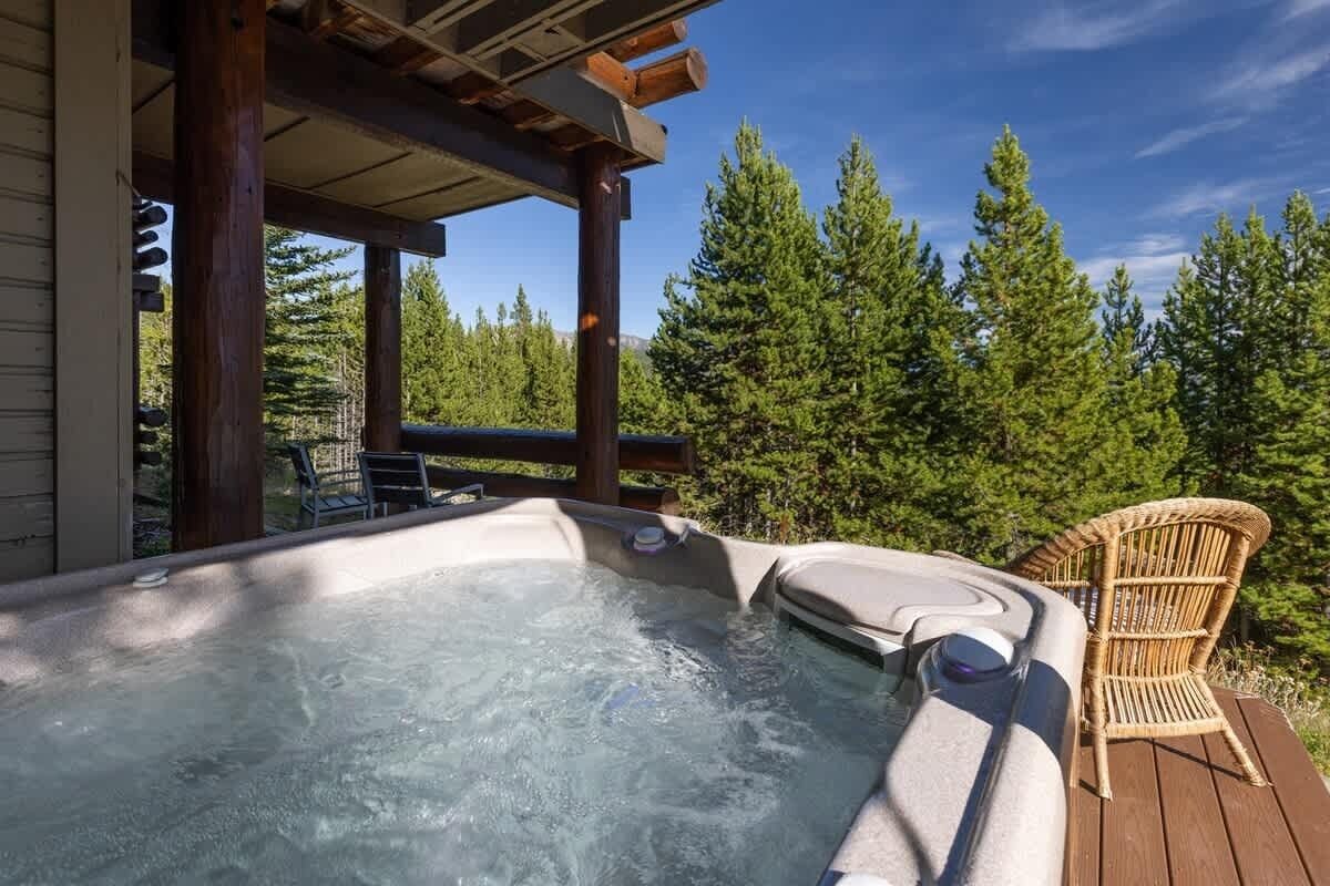 Ein Whirlpool mit Holzterrasse und Korbstuhl, umgeben von Bäumen.