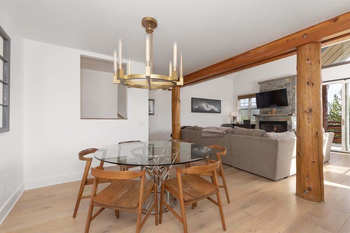 Una sala de estar moderna con una mesa de comedor de vidrio, sillas de madera, una chimenea de piedra y un ventanal grande.