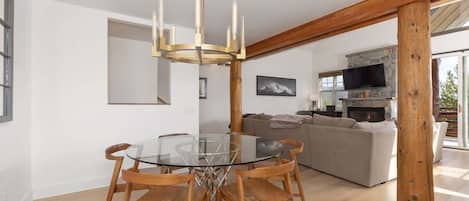 Una sala de estar moderna con una mesa de comedor de vidrio, sillas de madera, una chimenea de piedra y un ventanal grande.