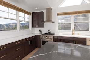 A modern kitchen with dark cabinetry, a large island, and a view of the mountains through the windows.