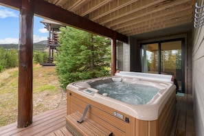 Un jacuzzi en una terraza de madera con vistas a un bosque y montañas al fondo.