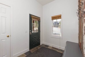 A hallway with a dark door, a window with a wooden blind, and a wall-mounted coat rack.