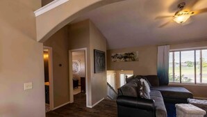 Un salon spacieux doté d’un parquet en bois foncé, d’un canapé en cuir noir et d’un ventilateur de plafond.