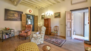 A cozy living room with wooden floors, a bookshelf, a floral armchair, a traditional wooden cabinet, and a painting on the wall.