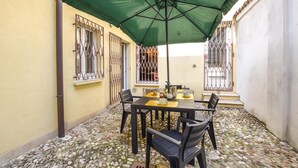 An outdoor patio with a table and chairs, a green umbrella, and a stone-tiled floor.