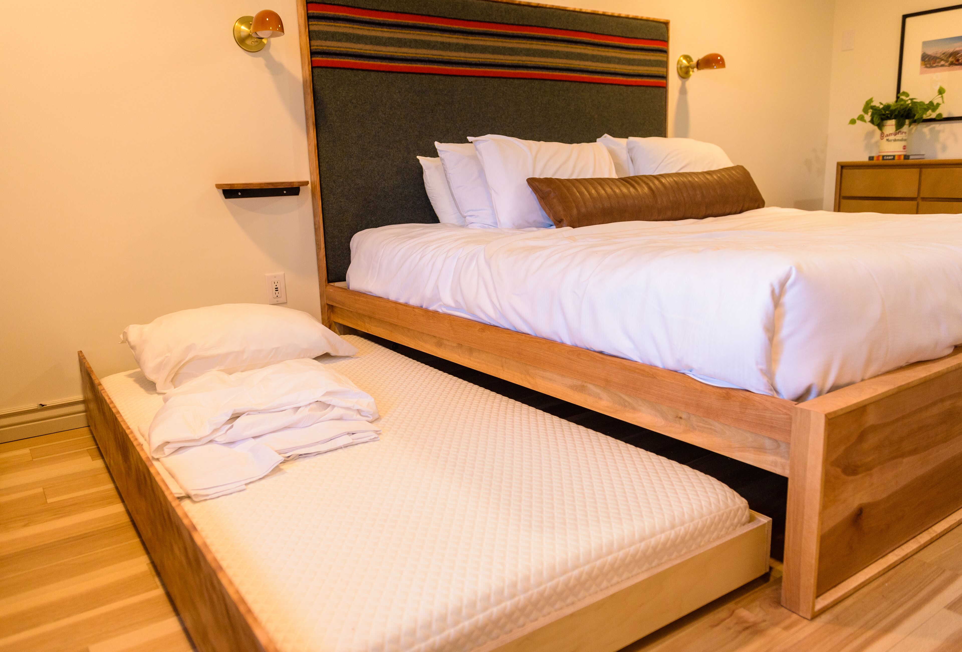 A double bed with a wooden frame, a headboard with a striped design, and a bedside table with a lamp.