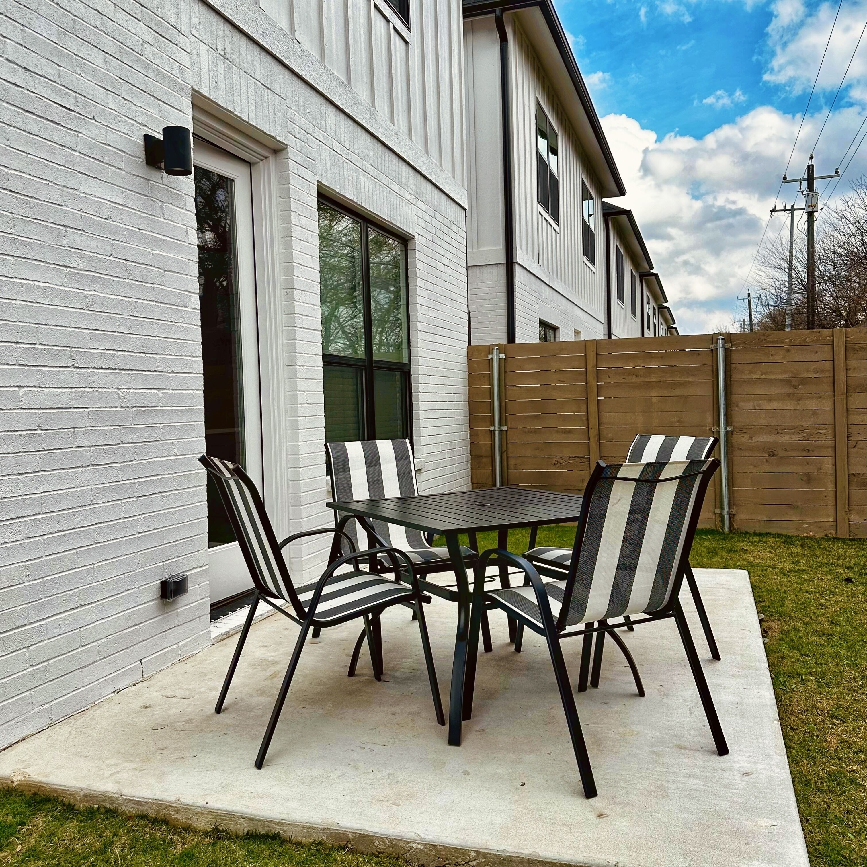 Un patio con una mesa y sillas, un muro de ladrillo blanco y una cerca de madera.