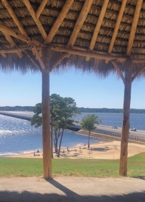 Un pavillon en bois, doté d’un toit de chaume, qui offre une vue sur une plage et l’océan.