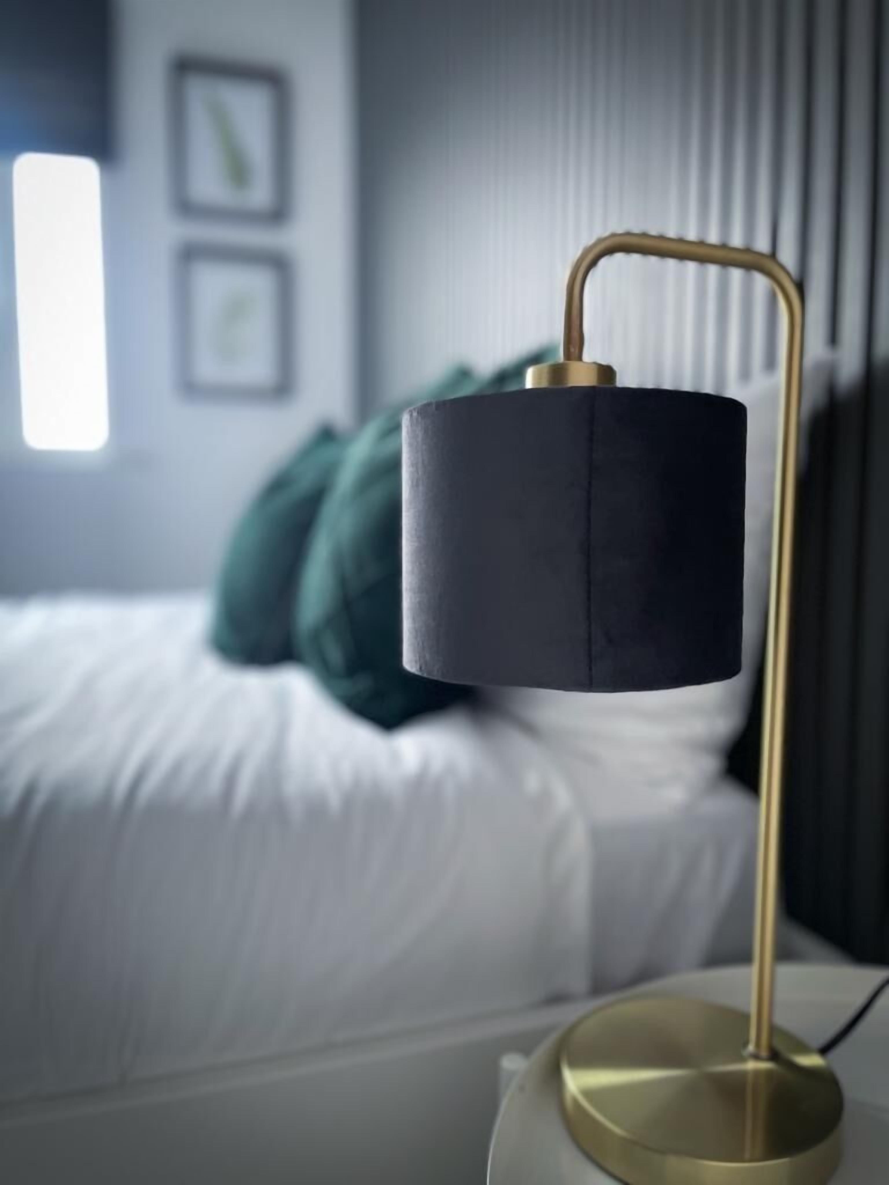 A modern bedroom with a bed, a bedside table with a lamp, and a window.