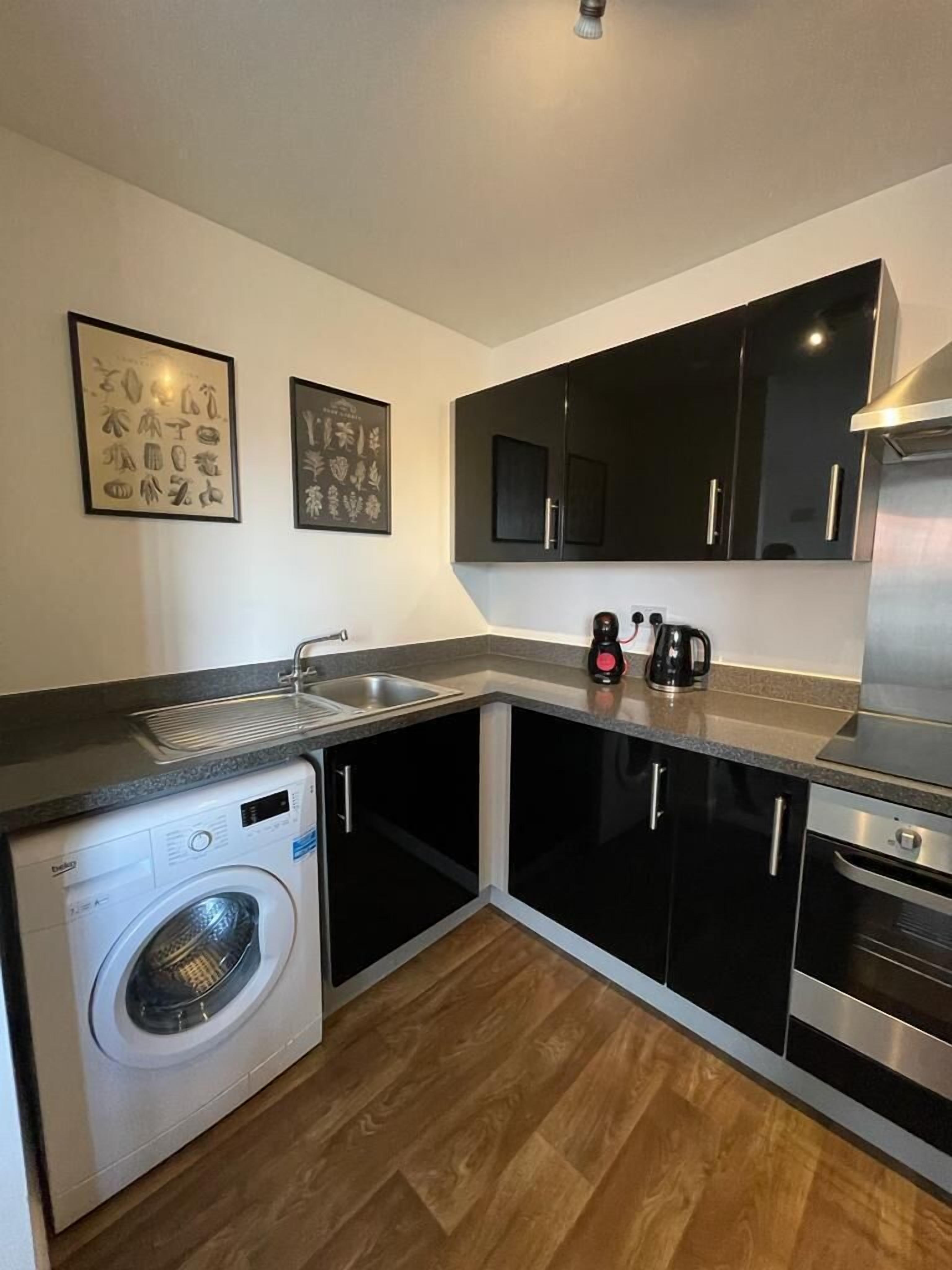A compact kitchen with a washing machine, a coffee maker, and a built-in oven.