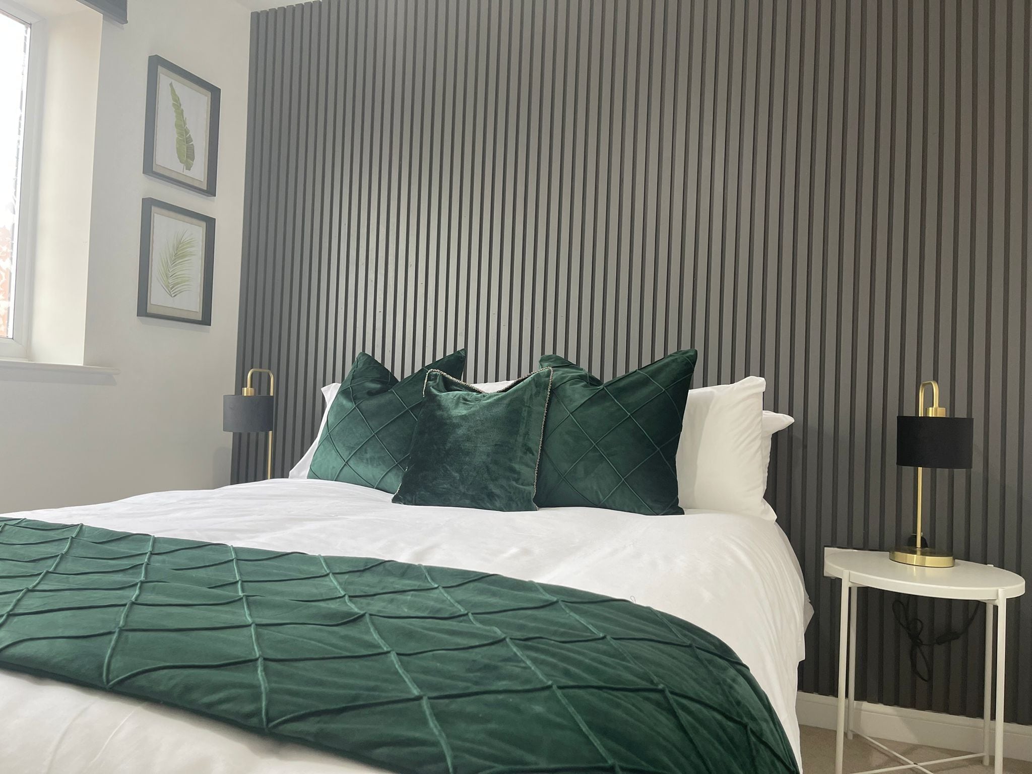 A modern bedroom with a bed, green and white bedding, a striped wall, and two bedside lamps.