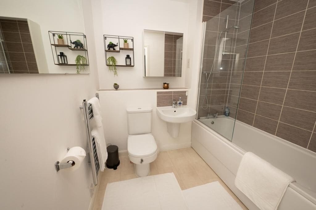 Une salle de bain moderne équipée de toilettes, d’un lavabo et d’une douche. On y trouve des étagères avec des plantes et un miroir au-dessus du lavabo.
