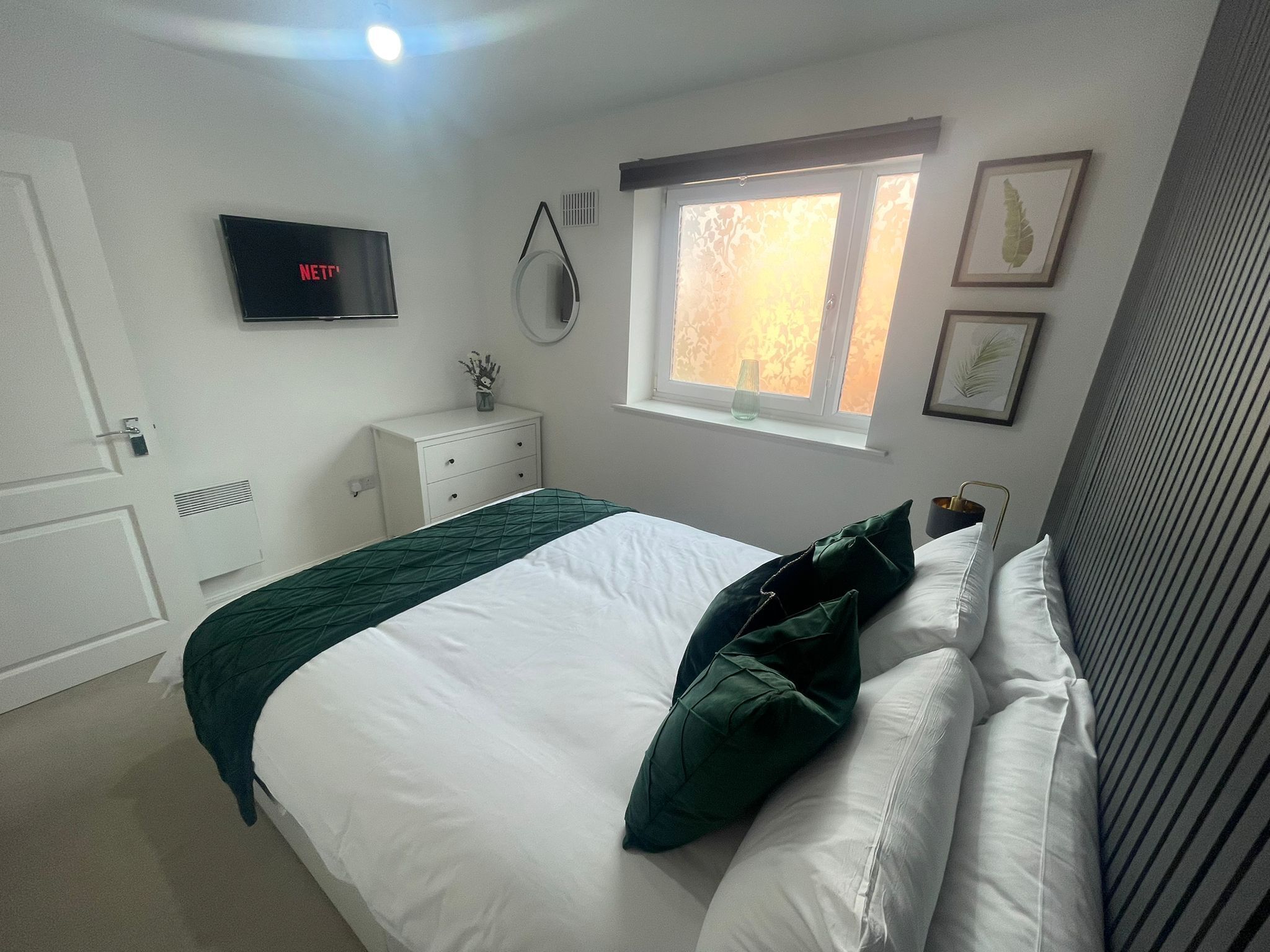 A bedroom with a bed, a dresser, a TV, a window, and framed pictures on the wall.
