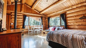 A log cabin interior with a bed, a desk, and a table. - Pet-Friendly Off-grid Log Cabin, Hiking, Mountain Air and Dark Skies Await! (Rock Lake Provincial Park)