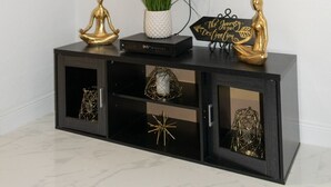 A black entertainment unit with a television mounted above it, a potted plant, and decorative items including golden statues and a sign. - Entire Condominium Home away from Home with Pool, Near Beach (Nassau)