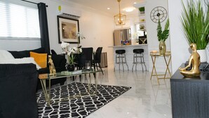 A modern living room with a black and white patterned rug, a glass coffee table, black sofas, and a dining area with bar stools. - Entire Condominium Home away from Home with Pool, Near Beach (Nassau)