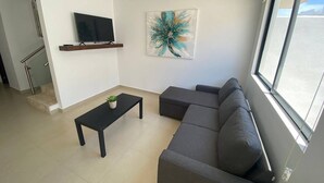 Un salon moderne avec un canapé gris, une table basse noire, un téléviseur fixé au mur et un grand tableau abstrait.