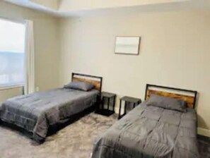 Two single beds with headboards and matching pillows, a small table, and a wall-mounted shelf.