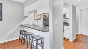 A modern kitchen with a central island, bar stools, and a microwave.