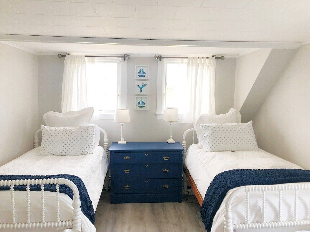 Ein Schlafzimmer mit zwei Einzelbetten, einer blauen Kommode und einem Fenster mit Vorhängen.