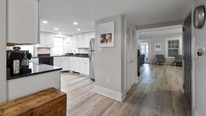 A spacious kitchen with white cabinets, a wooden bench, and a dining area with a view of the living room. - Updated Biddeford Pool Beach House (Biddeford)