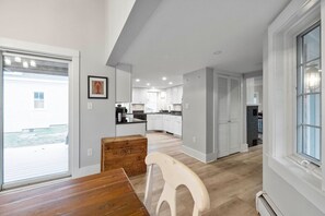 Une cuisine moderne avec des meubles blancs, une table à manger en bois et une vue sur le jardin à travers une porte-fenêtre coulissante.