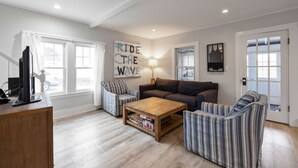 A living room with a sofa, two striped armchairs, a coffee table, and a TV on a wooden stand. - Updated Biddeford Pool Beach House (Biddeford)