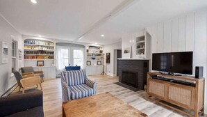 A modern living room with a sofa, armchairs, a coffee table, a fireplace, a TV, and built-in bookshelves. - Updated Biddeford Pool Beach House (Biddeford)