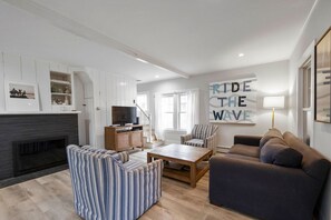 Un salon moderne doté d’une cheminée, d’un téléviseur et d’une grande œuvre d’art murale sur laquelle on peut lire : « SURFEZ SUR LA VAGUE ».