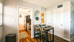 A compact kitchen with a dining area, a trash bin, and a small rug.