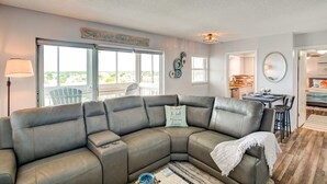A living room with a sectional sofa, a dining area with a table and chairs, and a view through large windows.